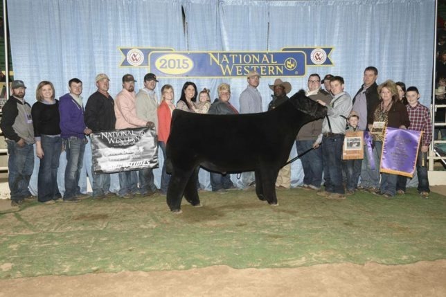 Andrew Hodges of Coffey County showed this champion at the National Western Livestock Show in Denver, and it was a happy occasion for Dylan Evans (just behind the winning exhibitor), wife Chelsea, the Hodges and Holmes families and many friends as all were smiles posing for the win picture.