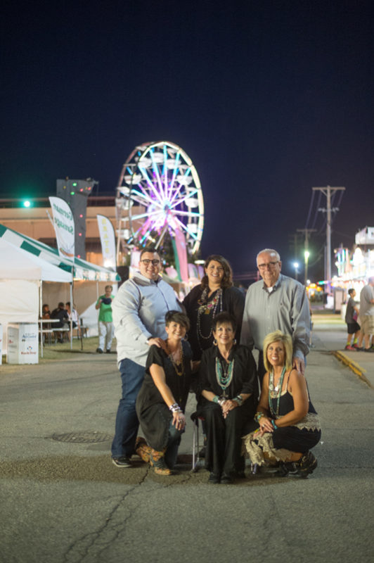 State Fair Time is family time and everybody gets involved when Dylan Evans of Lebo assists a large group of young people with their projects during competitions. But, there’s still time to take in other fair festivities, as Dylan and his wife Chelsea, his parents John and Sara, and his sisters Megan and Kate pose for a family portrait among the Midway color and action.