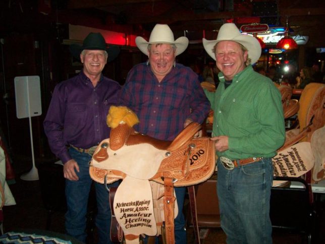 Bronco Billy Jim Hunter (center) was always biggest of smiles when presenting one of his custom made Bronco Billy trophy saddles as he is with champion amateur heeler Doc Lemmon and Zach Wiges, president Nebraska Roping Association.